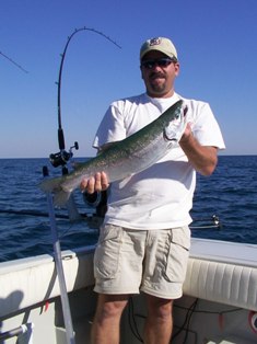 Photo of an angler holding a steelhead in front of downriggers.